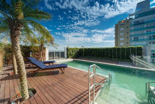 um deque com uma piscina num edifício com uma palmeira em Hotel Laghetto Stilo Higienópolis em Porto Alegre