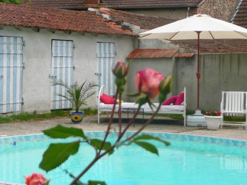a pool with an umbrella and two chairs and a table at Chambres d'hôtes et Roulotte Au Bonheur Du Parc in Le Breuil
