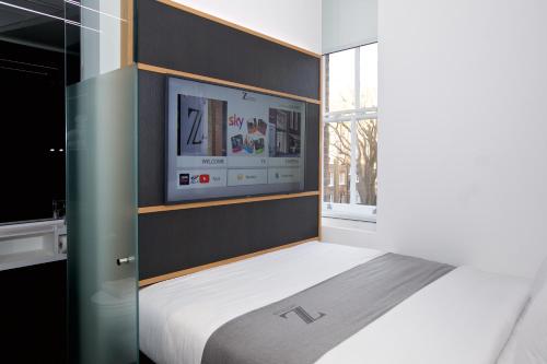 Un dormitorio con una cama con un televisor en la pared. en The Z Hotel Covent Garden, en Londres