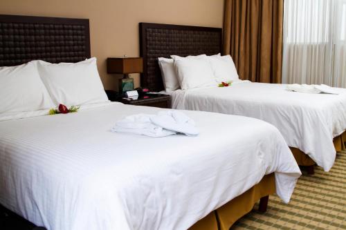 two beds in a hotel room with white sheets at Rincon del Valle Hotel & Suites in San José