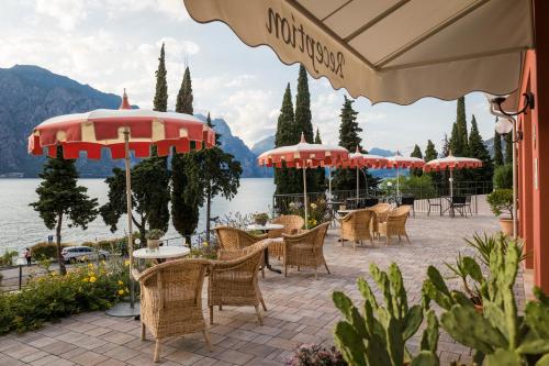 a patio with tables and chairs and umbrellas at Hotel Oasi Beach in Malcesine