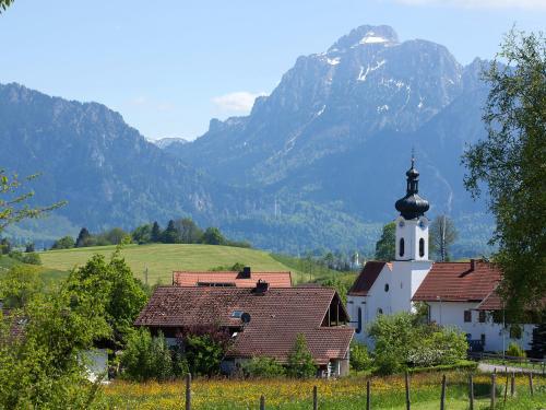a small white church with a steeple with mountains in the background at Gasthof Rössle in Rieden am Forggensee