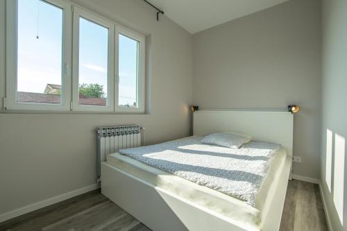 a white bedroom with a bed and two windows at Villa Gambera in Pirovac