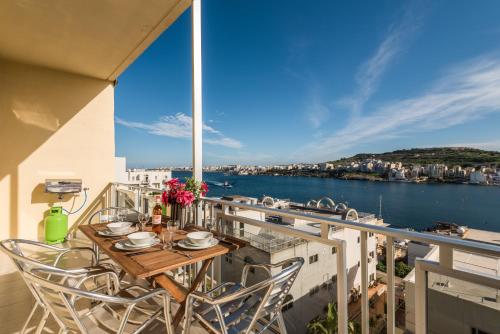 een balkon met een tafel en stoelen en uitzicht op het water bij Bayview 2 bedroom seaview apartment with large terrace with panoramic views - by Getawaysmalta in St Paul's Bay