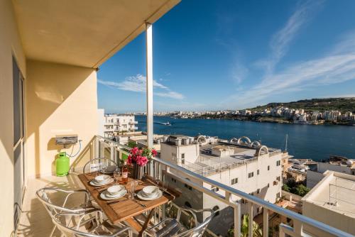 d'un balcon avec une table et des chaises et une vue sur l'eau. dans l'établissement Bayview 2 bedroom seaview apartment with large terrace with panoramic views - by Getawaysmalta, à San Pawl il-Baħar