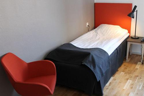 a bedroom with a bed and a red chair at Lindesbergs Stadshotell in Lindesberg