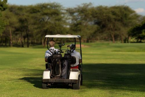 dois homens num carrinho de golfe num campo de golfe em Kili Villa Kilimanjaro Luxury Retreat em Arusha