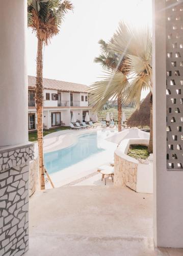a swimming pool with palm trees and a building at Kos One Hostel in Canggu