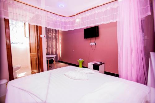 1 dormitorio con cama blanca y pared rosa en B10 Airport Lodge en Dar es Salaam
