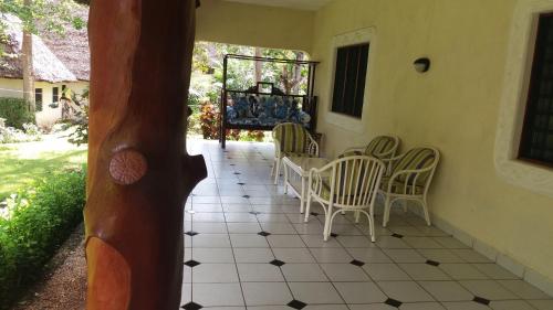 a porch with chairs and a table on a tiled floor at Diani Horizon Beach Cottages in Diani Beach