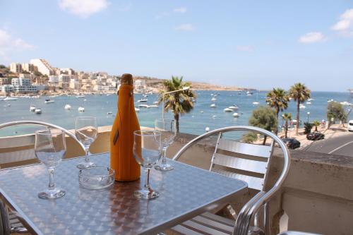 una mesa con copas y una botella de vino en el balcón en Blue Harbour 2 bedroom Seafront Apartments with large terrace with spectacular sea views - by Getawaysmalta, en St Paul's Bay