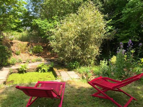 2 chaises rouges assises dans l'herbe dans un jardin dans l'établissement Manoir des petites bretonnes, à Saint-Quay-Perros