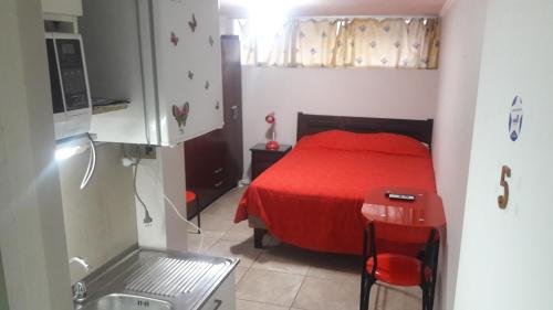 Dormitorio pequeño con cama roja y cocina en La Serena Mini Departamento, en La Serena
