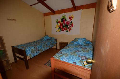 a bedroom with two beds and a painting on the wall at Camping Hostal Tipanie Moana Aeropuerto Centro in Hanga Roa