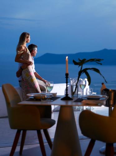 a man and woman standing next to a table at Santorini Princess Spa Hotel in Imerovigli