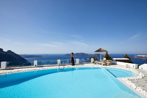 una donna è in piedi accanto a una piscina di Santorini Princess Spa Hotel a Imerovigli