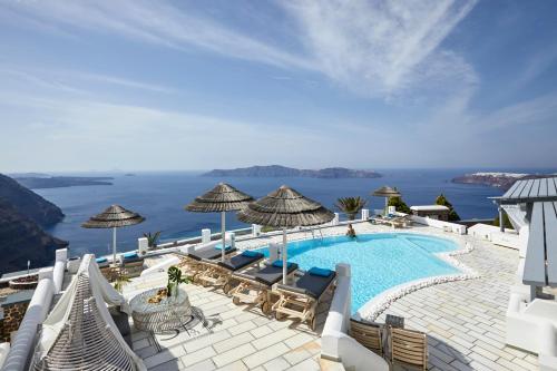 a pool with chairs and umbrellas and the ocean at Santorini Princess Spa Hotel in Imerovigli