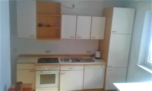 a kitchen with white cabinets and a sink and a refrigerator at Apartment MASCH in Arriach