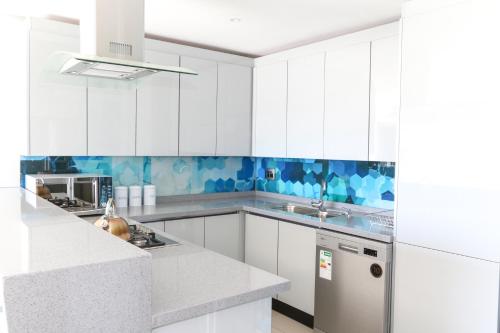 a white kitchen with white cabinets and blue tiles at GORDON's SHORE LUXURY APARTMENTS - Solar Powered in Gordonʼs Bay