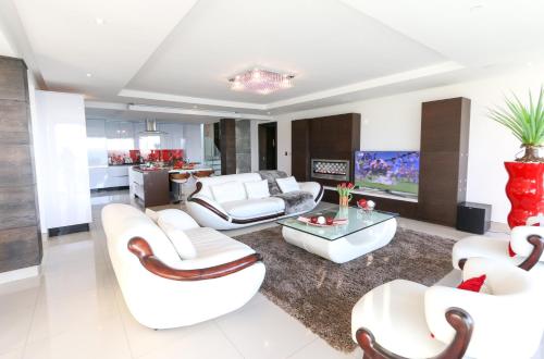 a living room with white furniture and a kitchen at GORDON's SHORE LUXURY APARTMENTS - Solar Powered in Gordonʼs Bay