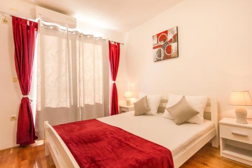 a bedroom with a white bed with red curtains at Apartments Spalato in Podstrana