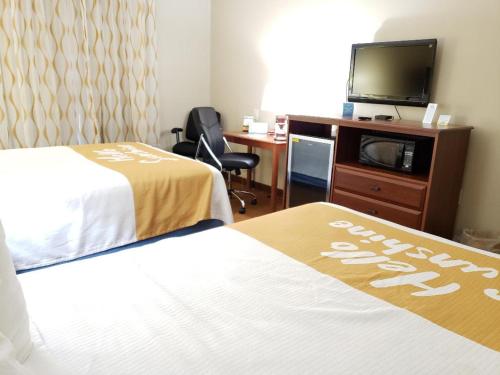 a hotel room with two beds and a desk and a tv at Days Inn by Wyndham Greensboro NC in Greensboro