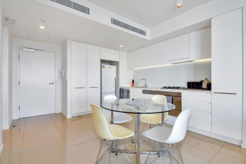 a white kitchen with a glass table and white chairs at Darwin Waterfront Short Stay Apartments in Darwin
