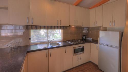 a kitchen with white cabinets and a sink and a refrigerator at Moama Riverside Holiday Park in Moama