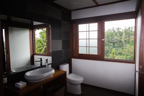 a bathroom with a sink and a toilet and two windows at Suarapura Resort & Spa in Tegalalang