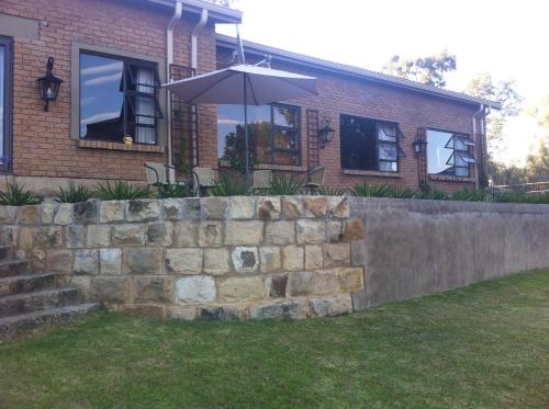 a brick house with an umbrella and a retaining wall at The Fat Mulberry Guest Farm in Fouriesburg