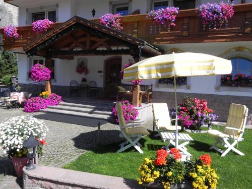 a patio with chairs and an umbrella and flowers at Hotel Garni Concordia - Dolomites Home in Selva di Val Gardena