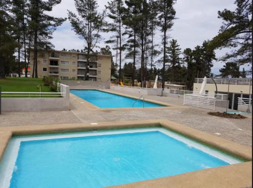 a large blue pool with a building in the background at Condominio Parquemar!!! in El Tabo