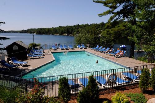 a large swimming pool with chairs and a lake at Rocky Crest Golf Resort in MacTier