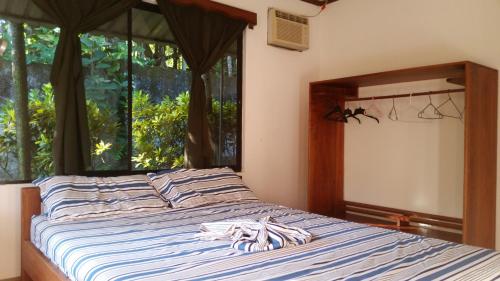 a bed with blue and white striped sheets and a window at Embassy House in Puerto Jiménez