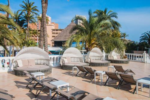 a patio with chairs and tables and palm trees at Magic Tropical Splash in Cala de Finestrat