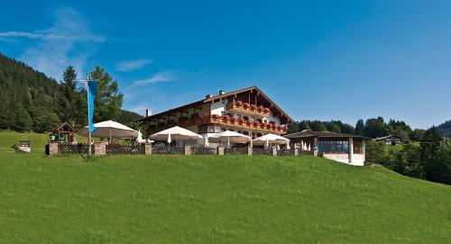 a building with umbrellas on a green hill at Hotel-Gasthof Nutzkaser in Ramsau