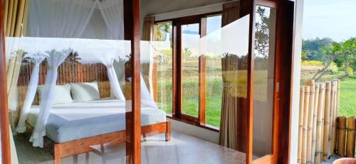 a bedroom with a bed and a large window at KUBU D'UME HOMESTAY in Jatiluwih