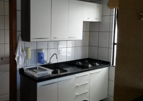 cocina con armarios blancos, fregadero y fogones en Apartamento em Meia Praia, Itapema, SC., en Itapema