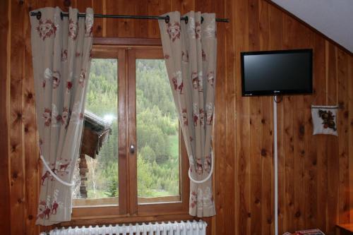a room with a window with curtains and a television at Hotel Le Chamois Logis in Molines-en-Queyras