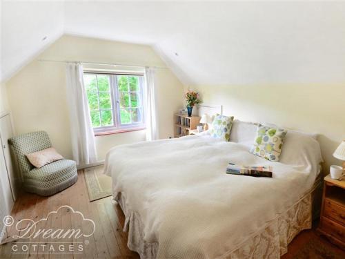 1 dormitorio con 1 cama blanca grande y 1 silla en Sixpenny Cottage, en Upwey