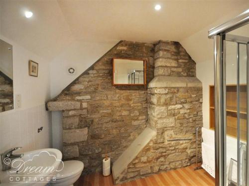 a bathroom with a stone wall with a sink and a toilet at Sixpenny Cottage in Upwey