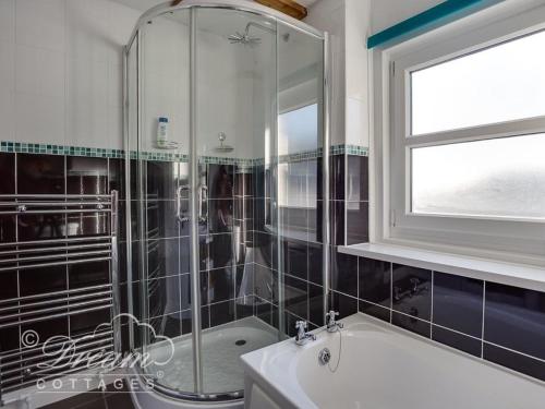 a bathroom with a shower and a tub and a window at Ammonite Cottage in Portland