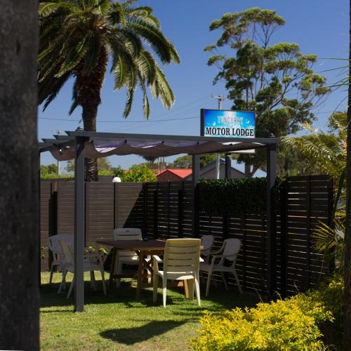 a table and chairs under a pergola with a sign at Tuncurry Motor Lodge in Tuncurry