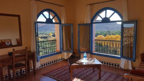 a living room with three windows and a table at Maison D'hotes Sahara in Aoufous
