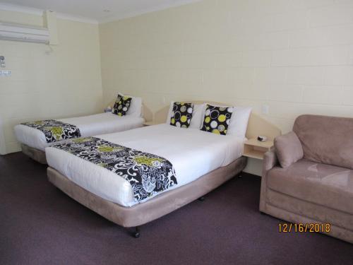 two beds in a room with a couch and a chair at Moruya Motel in Moruya