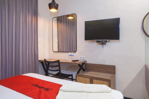 a hotel room with a bed and a desk with a television at RedDoorz @ Wiyung 2 in Kedurus