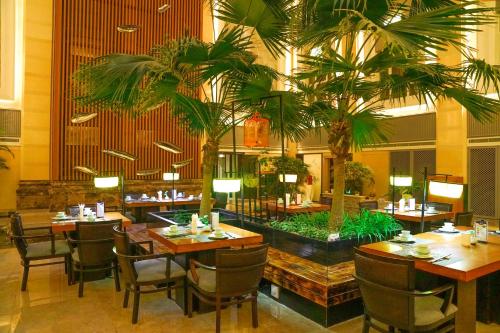 a restaurant with tables and chairs and palm trees at Yantai Meiya International ApartHotel (Previous Ramada Plaza) in Yantai