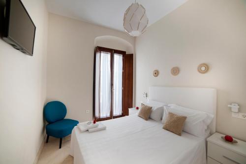 a white bedroom with a white bed and a blue chair at Patio de la Cartuja in Seville