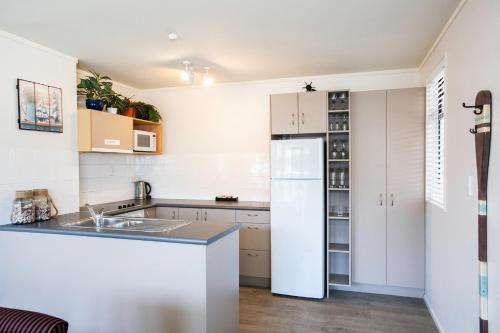 a kitchen with white cabinets and a white refrigerator at Capri on Pilot Bay in Mount Maunganui