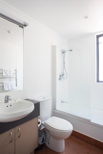 a white bathroom with a toilet and a sink at Capri on Pilot Bay in Mount Maunganui